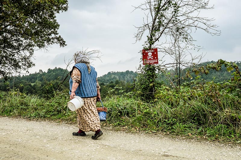 A village woman skirts a marked minefield on her way to pick berries