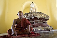 A monk ponders under Buddha's sculpture